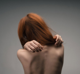 Giovane donna di spalle con la schiena scoperta, posa che esprime vulnerabilità e disagio.