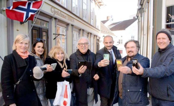 Foto di gruppo durante il meeting internazionale 'Promozione dell'integrazione' a Grimstad, Norvegia, 7-11 marzo 2022: sette persone sorridenti in strada, con smartphone, bandiera norvegese sullo sfondo.